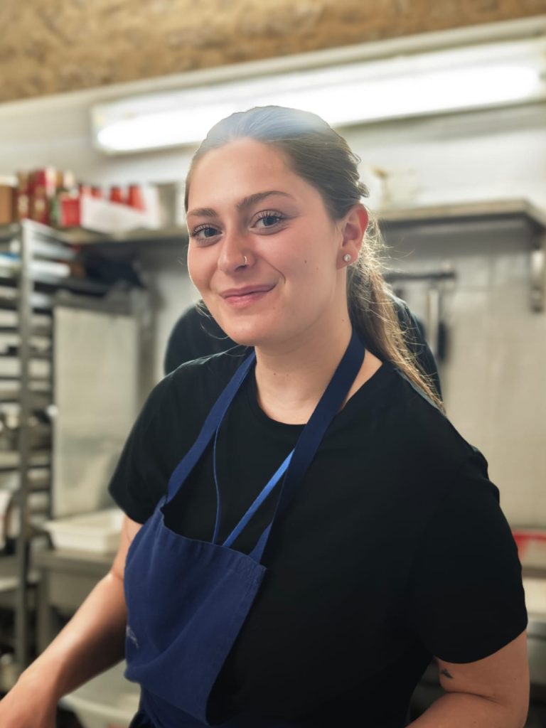 Chef Beth souriant dans une cuisine professionnelle.