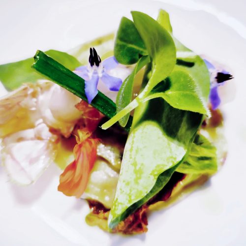 Plat de légumes verts et fleurs comestibles disposés artistiquement sur une assiette.