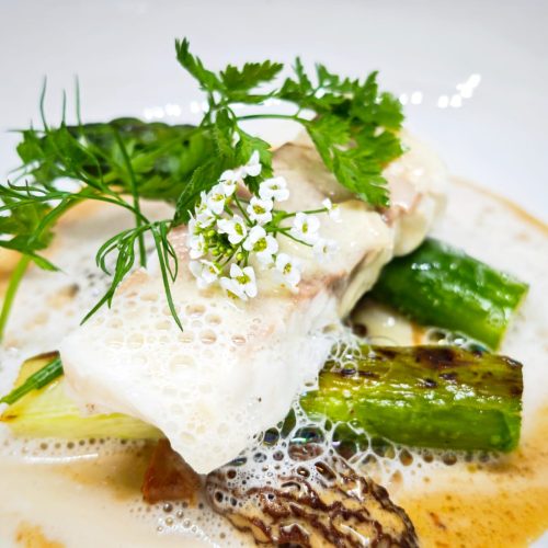 Plat de poisson avec légumes et sauce, décoré de fleurs comestibles.