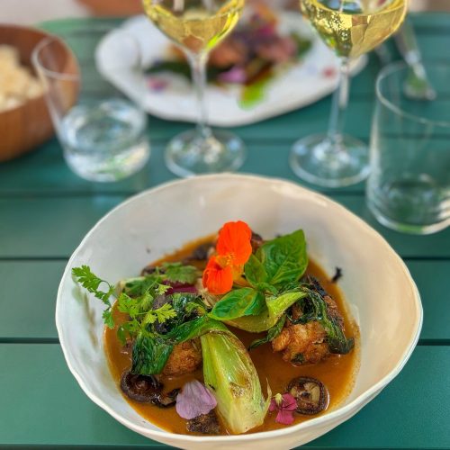 Un plat de viande avec sauce et légumes, accompagné d'un verre de vin blanc.