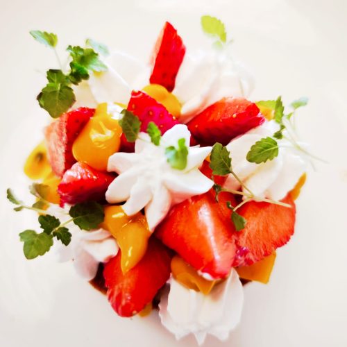 Salade de fruits colorée avec des fraises, des mangues et de la crème fouettée.